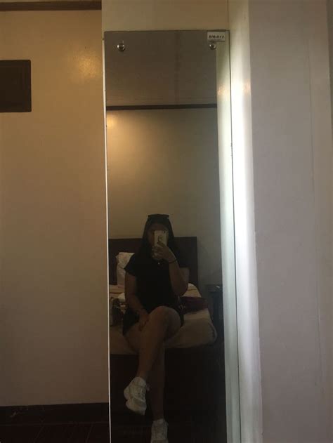 A Woman Taking A Selfie While Sitting On A Bed In A Room With White Walls