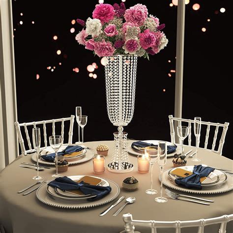 The Table Is Set With Plates Silverware And Pink Flowers In A Tall Vase