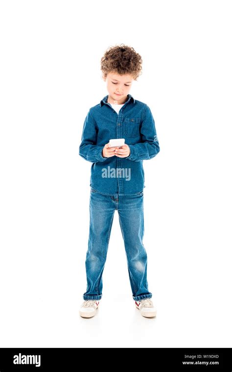 Full Length View Of Concentrated Kid In Denim Clothes Using Smartphone