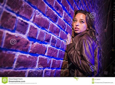 Frightened Pretty Young Woman Against Brick Wall At Night Stock Image
