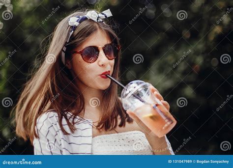 Happy Hipster Girl With Sunglasses In Retro Dress And Headband Holding Plastic Cup And Straw