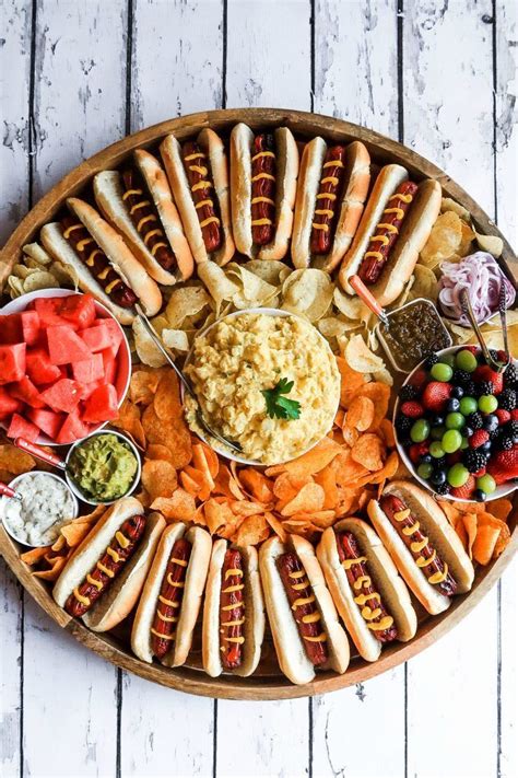 A Platter Filled With Hot Dogs Vegetables And Dips