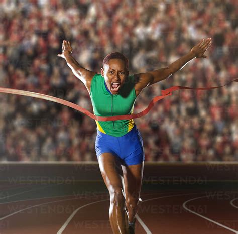 Young Woman Sprinting Through Winners Tape In Stadium Stock Photo