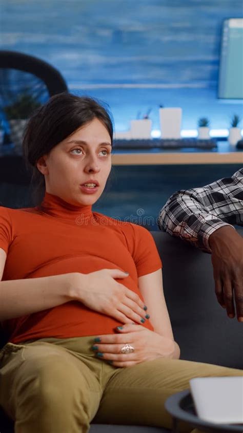 Interracial Couple With Pregnancy Relaxing On Couch At Home Stock Image