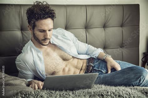 Sexy Handsome Man Laying With Open Shirt On His Bed With Laptop Computer Working Or Surfing The