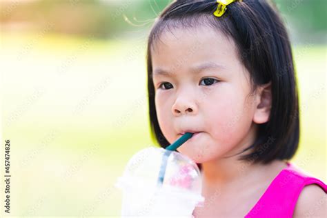 Cute Asian Girl Sucking Water From A Plastic Glass With A Green Straw On A Hot Day While Shes