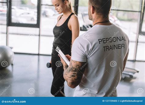 Rear View Of Male Personal Trainer With Clipboard And Young Sportswoman
