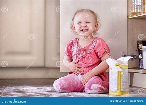 Playful Laughing Little Baby Girl Smeared In Flour Sits On The Kitchen
