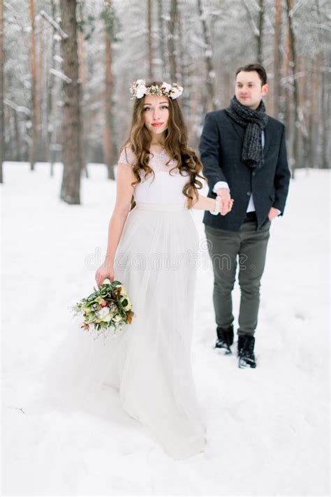 Winter Wedding Bride And Groom Hold Hands And Look At The Snowy Forest