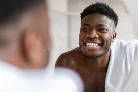 African Guy Looking At Toothy Smile In Mirror In Bathroom Stock Photo