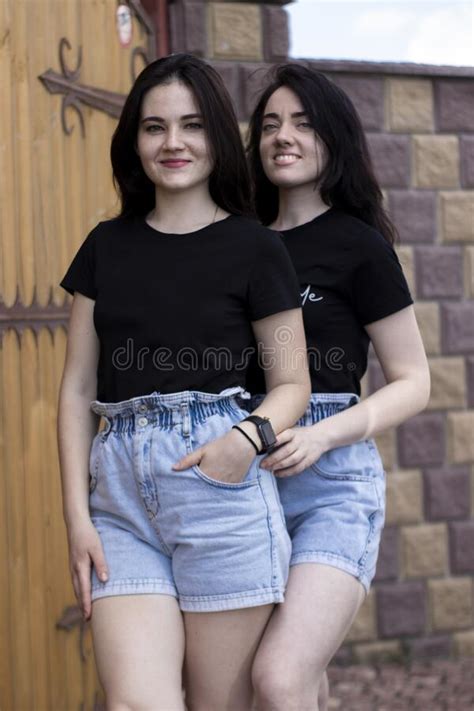 Two Young Brunette Women In A Black T Shirt And Denim Shorts Hugging
