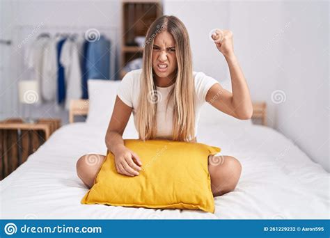 Young Blonde Woman Sitting On The Bed With Pillow At Home Angry And Mad