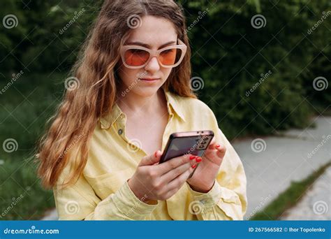 A Young Slender Girl In Sunglasses And A Yellow Shirt Holds A Mobile