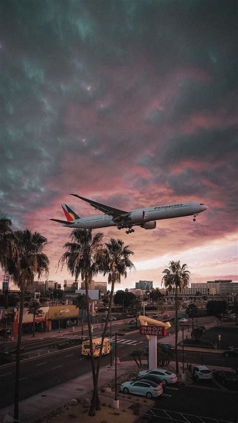 An Airplane Taking Off Into The Sky At Sunset With Palm Trees In The