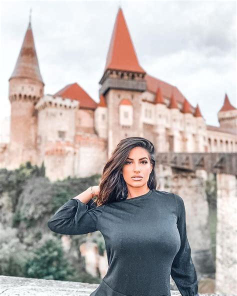 a woman standing in front of a castle with her hand on her hip and looking at the camera