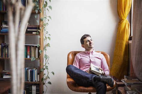 Thoughtful Man Holding Book While Sitting On Chair At Home Stock Photo