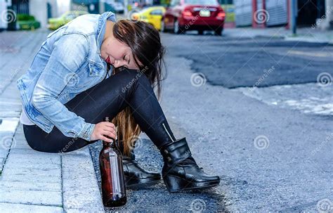 Beautiful Young Drunk Woman Sitting In A Sidewalk With Bottle Of Beer In Her Hand Sleeping