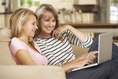 Mother With Teenage Daughter Sitting On Sofa At Home Using Lapto Moms