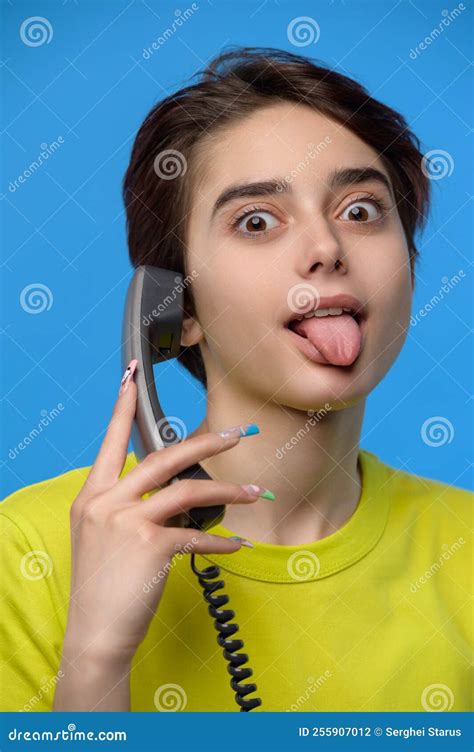 Beautiful Young Skinny Brunette Grimaces With Tongue Out While Talkng On Landline Phone Stock