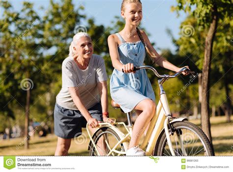 Positive Senior Woman Teaching Her Granddaughter Riding A Bicycle Stock