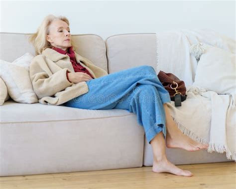 tired senior woman looking aside while resting on sofa at home after hard working day stock