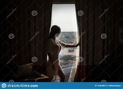 Young Pretty Woman Standing By A Window Looking Outside Expecting