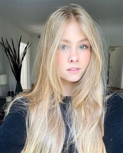 a woman with long blonde hair standing in front of a mirror looking at the camera