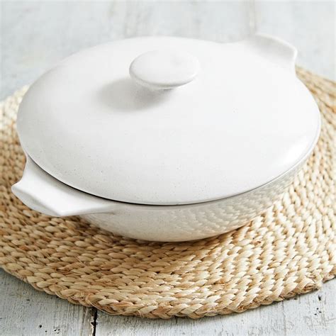 A White Bowl With A Lid Sitting On Top Of A Woven Place Mat Next To A
