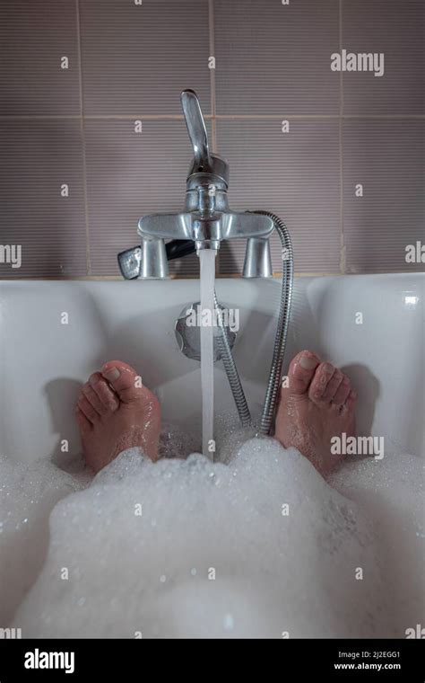 Male Feet Seen Sticking Out Of A Foam Bath In A Bathtub Water Is Flowing And A Man Is Relaxing