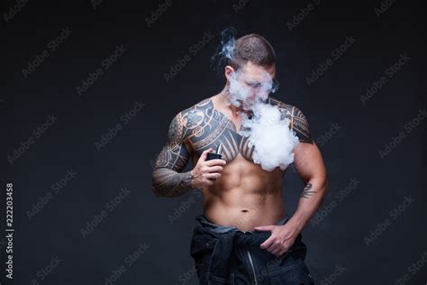 Vaper The Man With A Muscular Naked Torso With Tattoos Smoke An Electronic Cigarette On The