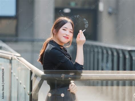 portrait of beautiful chinese girl in black dress smoking a cigarette outdoor in sunny day