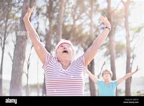 Senior Woman Stretching Arms Overhead In Yoga Class In Sunny Park Stock