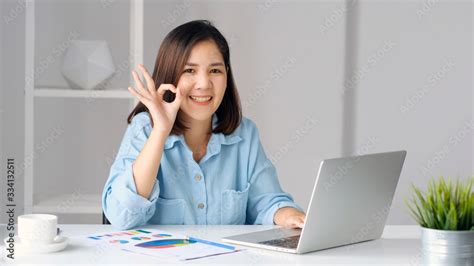 work from home happy asian women working with laptop computer at home office showing ok hand
