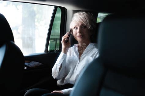 Cheerful Mature Woman In Business Suit Sitting On Backseat Of Her Car
