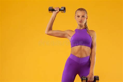 fitness woman athlete and bodybuilder holding dumbbell isolated on yellow background stock