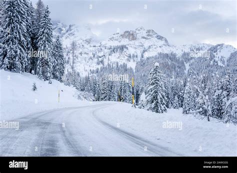 Snowy Winding Mountain Road At The Foot Of Towering Mountain Peaks In