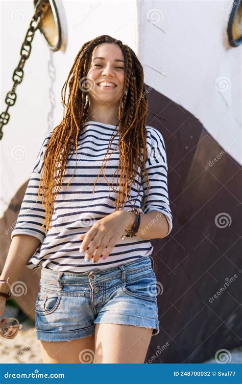 A Girl With A Dreadlocked Hairstyle Poses On The Beach Near A Ship In
