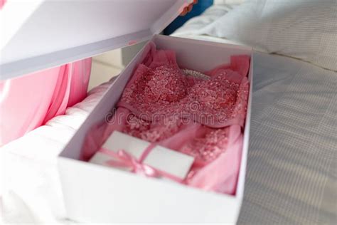 A Young Girl In A Pink Robe Opens A White Box With A Bow With A New