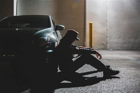 Anonymous Upset Young Guy Sitting On Ground Leaning On Car Tire · Free