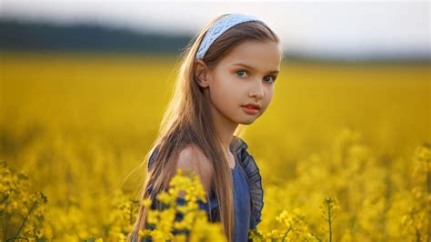 Cute Little Girl Is Sitting In Yellow Flowers Field Wearing Blue Frock