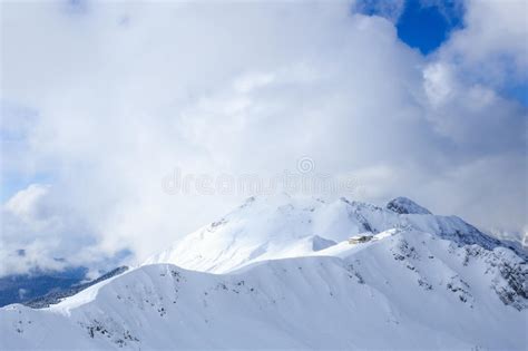 Building On The Top Of Snowy Mountain Ridge In The Sunlight And Clouds