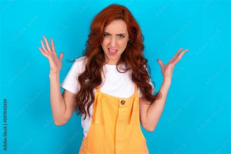 Crazy Outraged Young Redhead Woman Wearing Orange Overall Over Blue