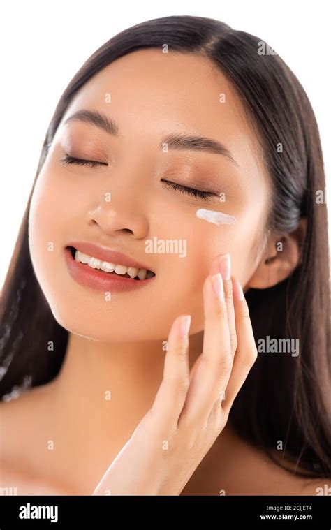 Brunette Asian Woman With Closed Eyes Applying Cosmetic Cream On Face Isolated On White Stock