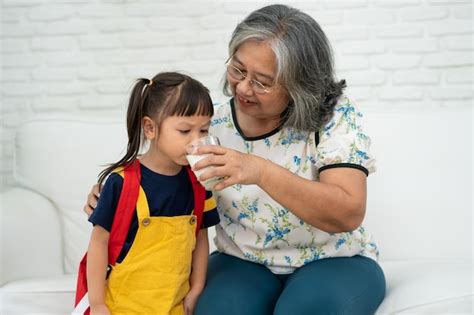 premium photo happy elderly asian grandma sits beside her granddaughter and feeds fresh milk