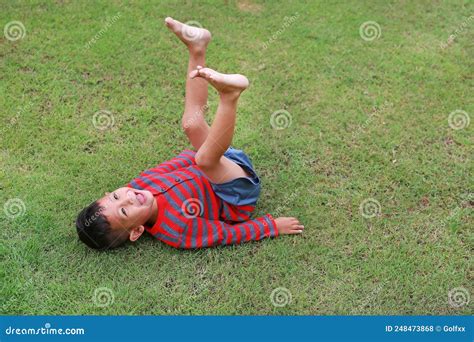 Adorable Asian Little Boy Lying On Grass With Lift Up His Legs At The