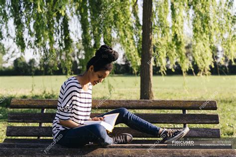 Young Woman Sitting On Park Bench Reading A Book — Meadow Adult