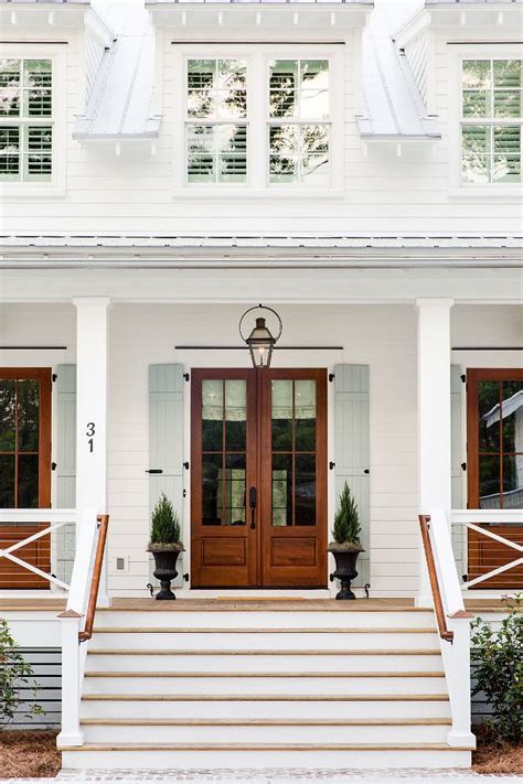 The exterior of the modern home with stone walls, large picture windows and red painted beams. Coastal Farmhouse | White farmhouse exterior, House ...
