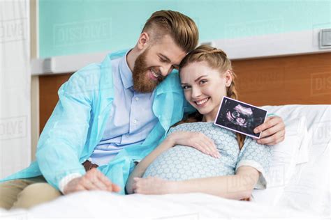 Pregnant Woman With Husband Hugging And Holding Sonogram In Hospital Stock Photo Dissolve
