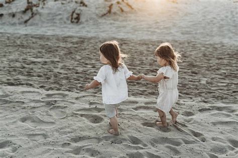 Side View Of Young Toddler Girls Holding Hands And Walking At Beach