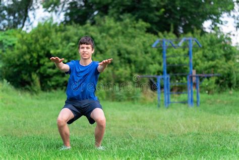 Teenage Boy Exercising Outdoors Sports Ground In The Yard He Squats